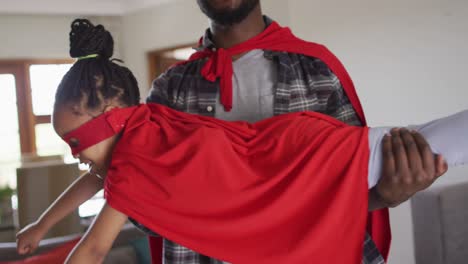 padre e hija afroamericanos felices divirtiéndose, vistiendo trajes de superhéroes.