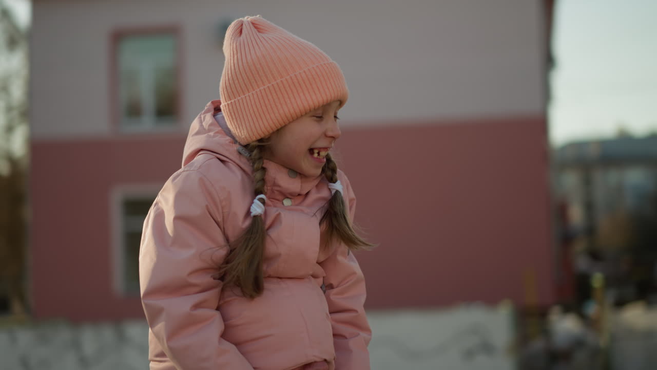 A little girl in a pink cap and jacket sits joyfully on her dad's neck, with half of his head snugly tucked in her jacket as she smiles brightly