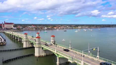 Toma-Aérea-De-4k-Del-Tráfico-Que-Pasa-Por-El-Puente-De-Los-Leones,-Frente-Al-Fuerte-Español,-Monumento-Nacional-Castillo-De-San-Marcos-Con-Cielos-Azules-Y-Nubes-Intermitentes