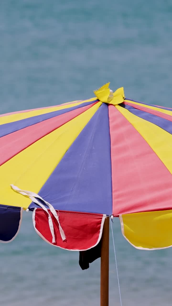 Un vivace ombrellone da spiaggia ondeggia dolcemente al vento contro uno sfondo oceanico sereno, catturando l'essenza di una giornata ventilata a Phuket.
