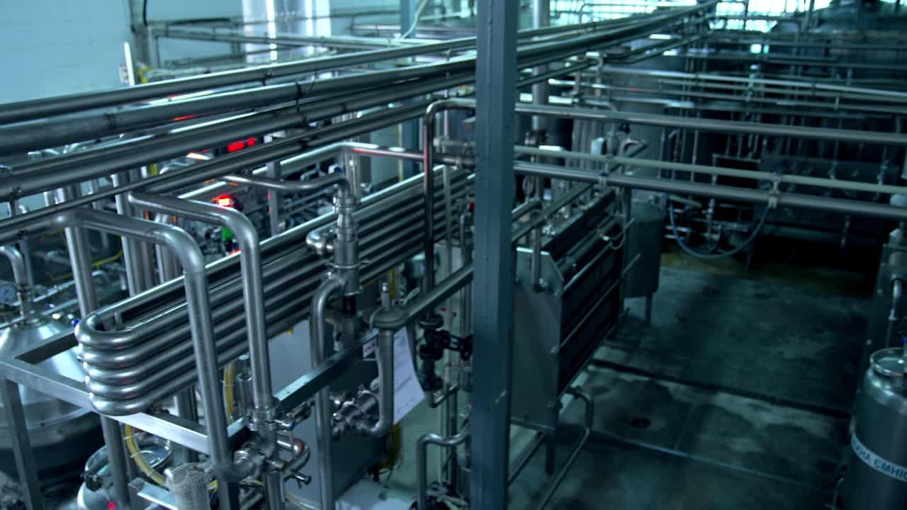 Milk and water pipelines at a modern dairy factory. Tanks, pipes and faucets close up. Gradual lifting above the factory equipment.