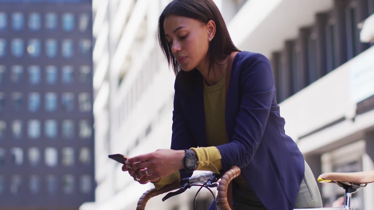African american woman using smartphone in street leaning on bicycle
