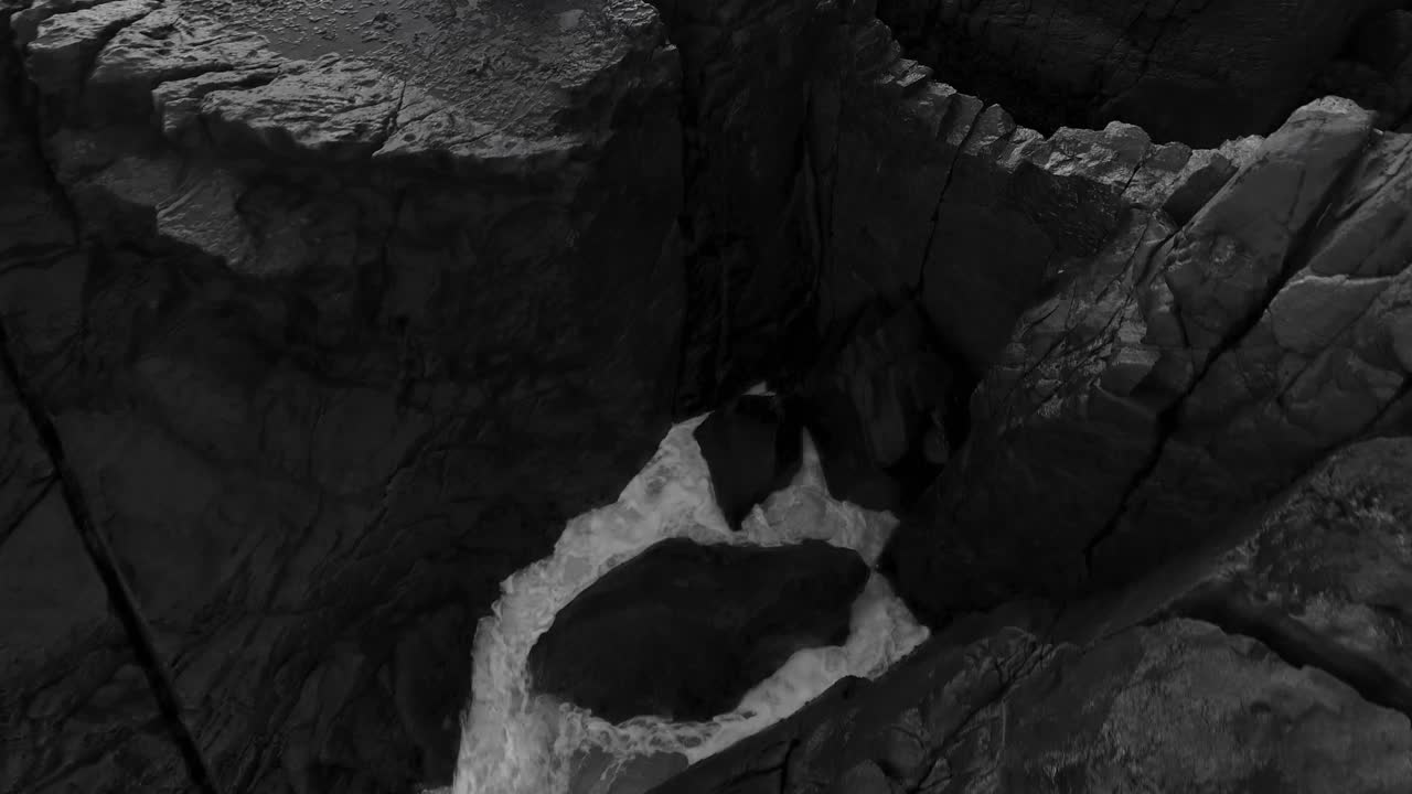 Ocean waves crashing against rock wall black and white