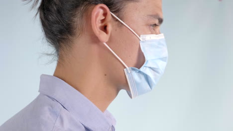 Man-facing-right-puts-on-blue-face-mask,-Extreme-Closeup-Profile