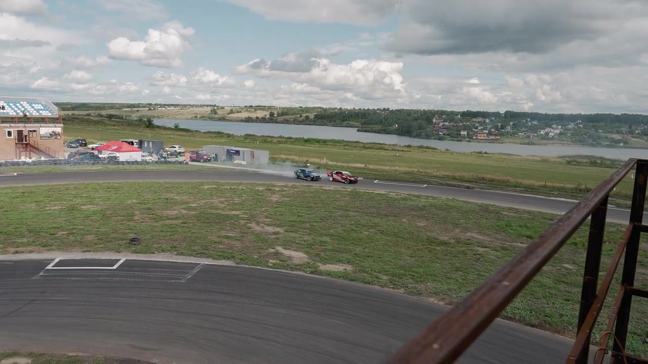 Højvinkelbillede af to sportsvogne, der drifter på en udendørs racerbane og producerer røg