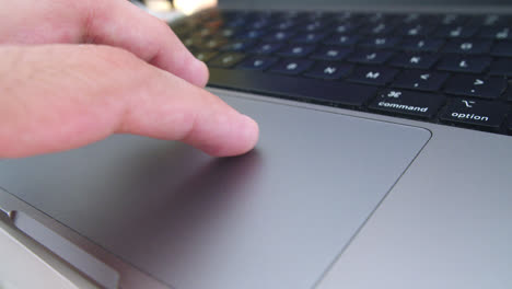 increíble close-up de cámara lenta de la mano de un joven operando el trackpad de su computadora macbook pro mientras busca información y trabaja desde casa por la tarde