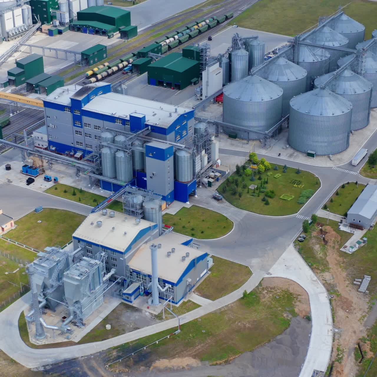 New agriculture complex on field. Modern granary for drying seed. Exterior of industrial factory with grain elevators, buildings and freight trains. View from above