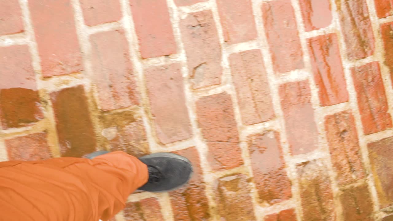 Action shot focusing on the movement of a foot (in a black boot) against the rough texture of wet bricks and bright orange clothing