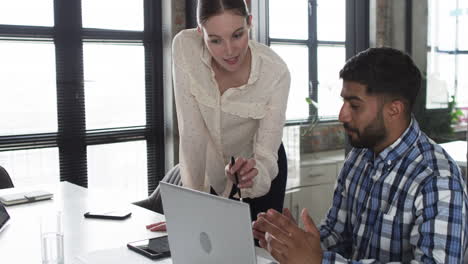 Young-Caucasian-woman-and-Asian-man-collaborate-over-a-laptop-in-a-business-office