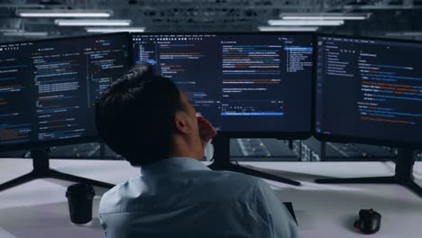 programmer working on multiple monitors in server room at night