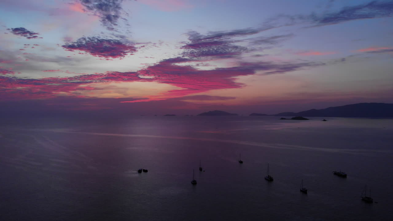 vista aérea de una colorida puesta de sol sobre el océano con barcos y montañas en el fondo