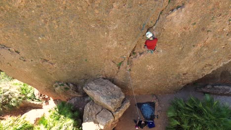 Man-rock-climbing-aerial-view-of-sportsman-rapelling-mountain-in-La-Panocha,-el-Valle-Murcia,-Spain-woman-rapel-down-a-mountain-climbing-a-big-rock