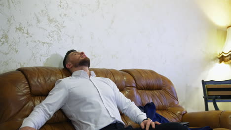 young handsome man in white shirt rests on a sofa in a hotel room. businessman moved in a hotel during business trip. modern hotel interior.