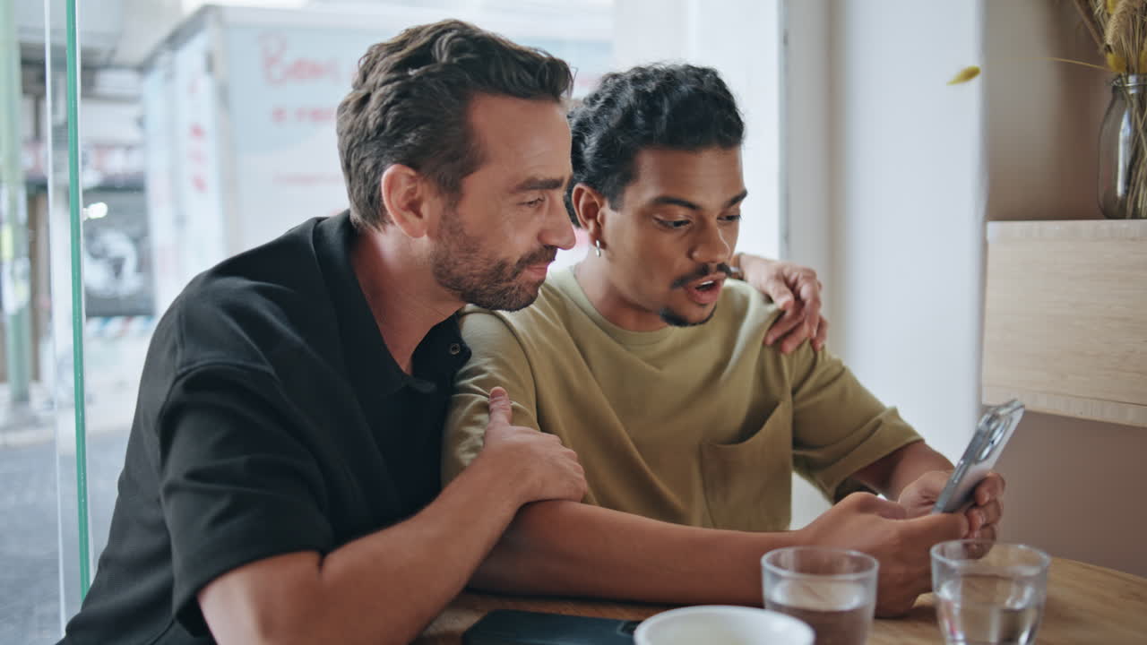 똑같은 섹스 연인들은 웃으며 휴대전화 화면을 보고 커피에 앉아 있습니다.