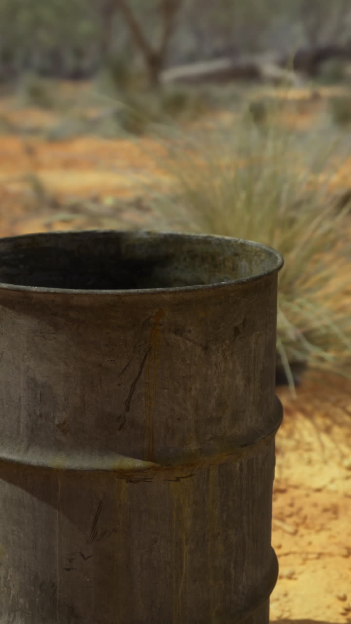 Rusty barrel amidst arid landscape with scattered rocks and sparse vegetation