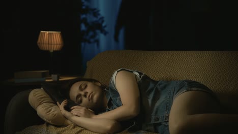 girl calmly sleepping on the sofa in the dark living room man maniac in hockey mask standing near - horror movie scene in the apartment creative concept. girl calmly sleepping on the sofa in the dark living room, man maniac in hockey mask standing near the window with knife, turns to the camera