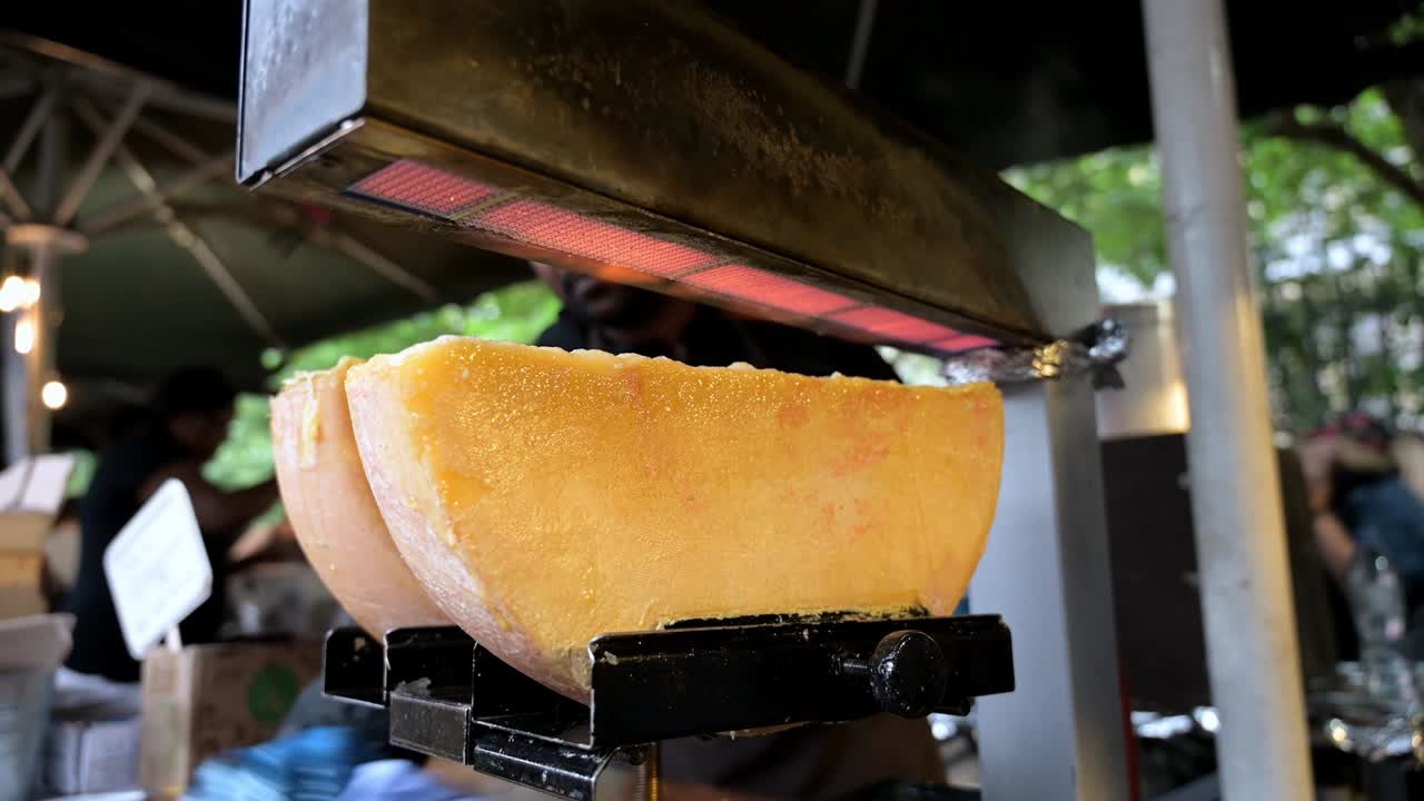 녹은 치즈가 반바의 치즈 래클에 거리는 불꽃 아래 런던의 보로 마켓의 거리 음식 상점에서 거품을 고 있습니다.