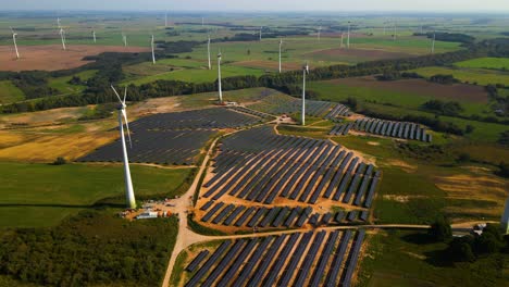 aerial footage of solar panels plant and wind turbines in a wind farm generating green electric energy on a wide green field on a sunny day, in taurage, lithuania, parallax