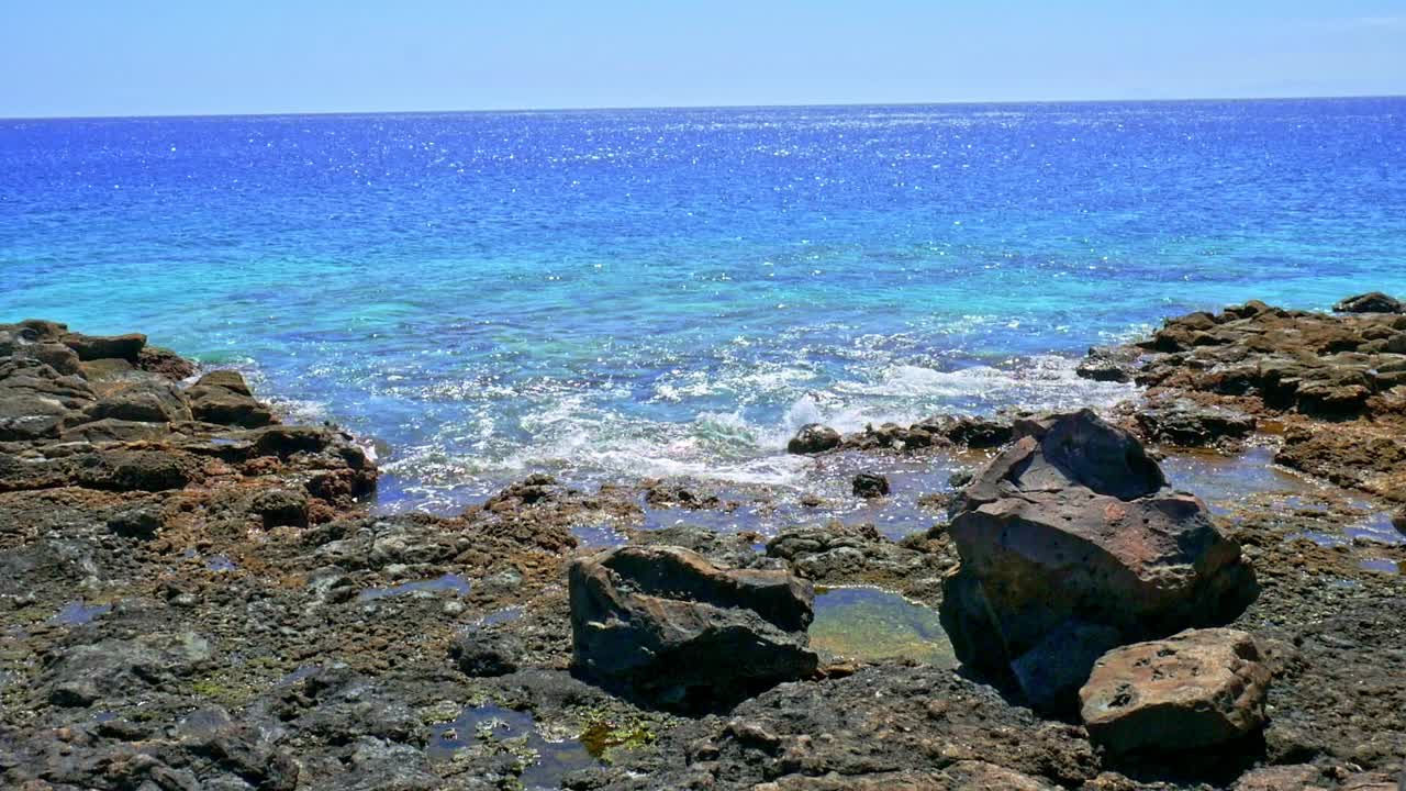 Wide slow motion shot of deep blue ocean gently breaking waves against a rocky shoreline in Lanzarote
