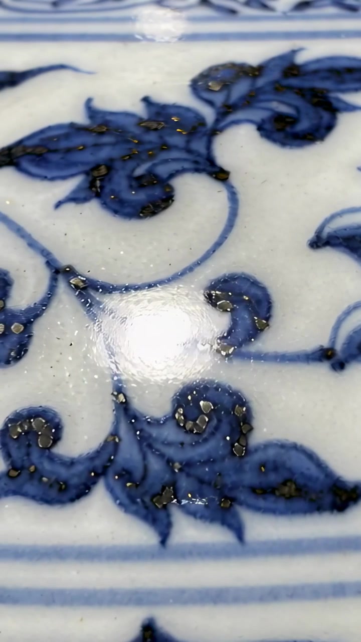 Dikey video: Eğildikten sonra mavi-beyaz sırlı seramik üzerine yayılan beyaz boncuk, altın pırıltılar görülüyor