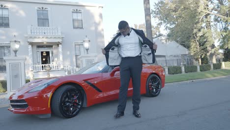 groom being photographed next to a red corvette on his wedding day