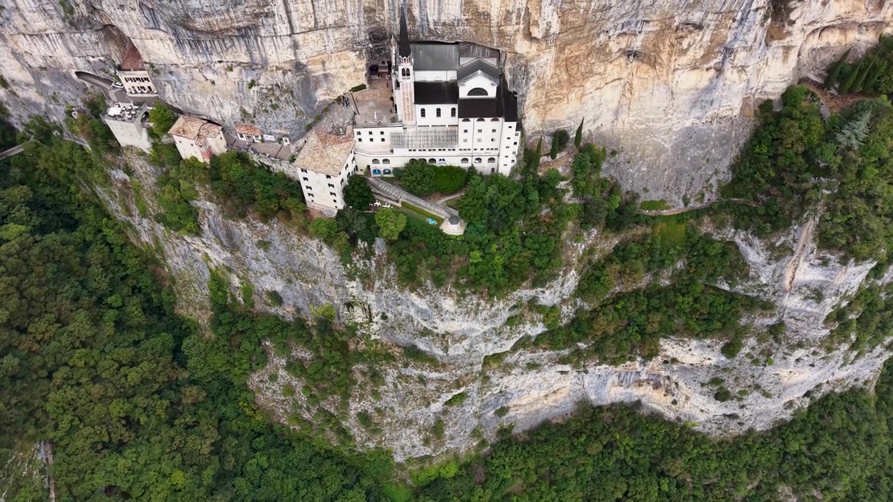 Drone footage showcasing Santuario Madonna della Corona perched on a towering limestone cliff above the forest in northern Italy