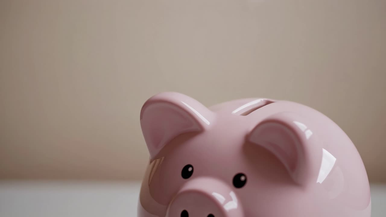 Close-up, eye-level shot of a pink piggy bank with a coin dropping in, symbolizing savings