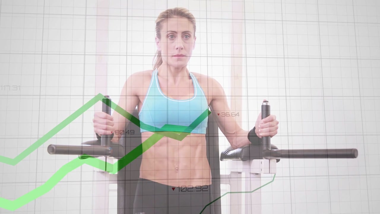 Fit woman gripping handles and raising legs on dip station with green overlay tracking fitness data