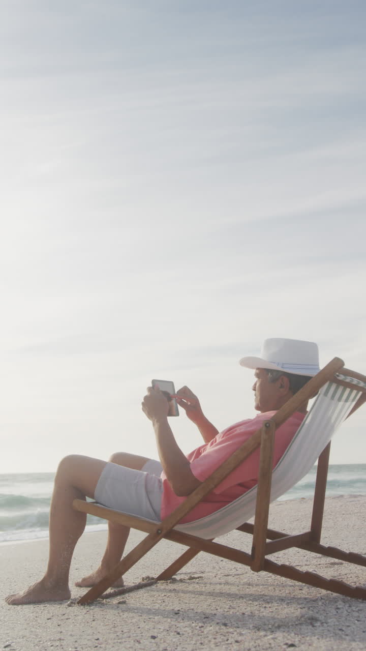 video vertical de un hombre biracial solo en una cama de sol en una playa soleada