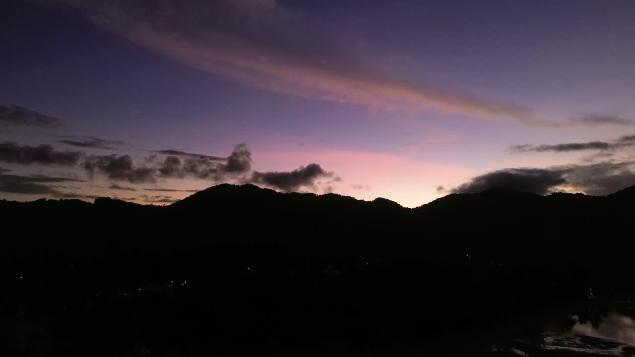 Drone footage capturing sunrise over Koh Phangan Thailand with the dark silhouette of a mountain and the reflection of it shimmering on the calm tropical sea