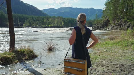 woman artist painting by a river in the mountains
