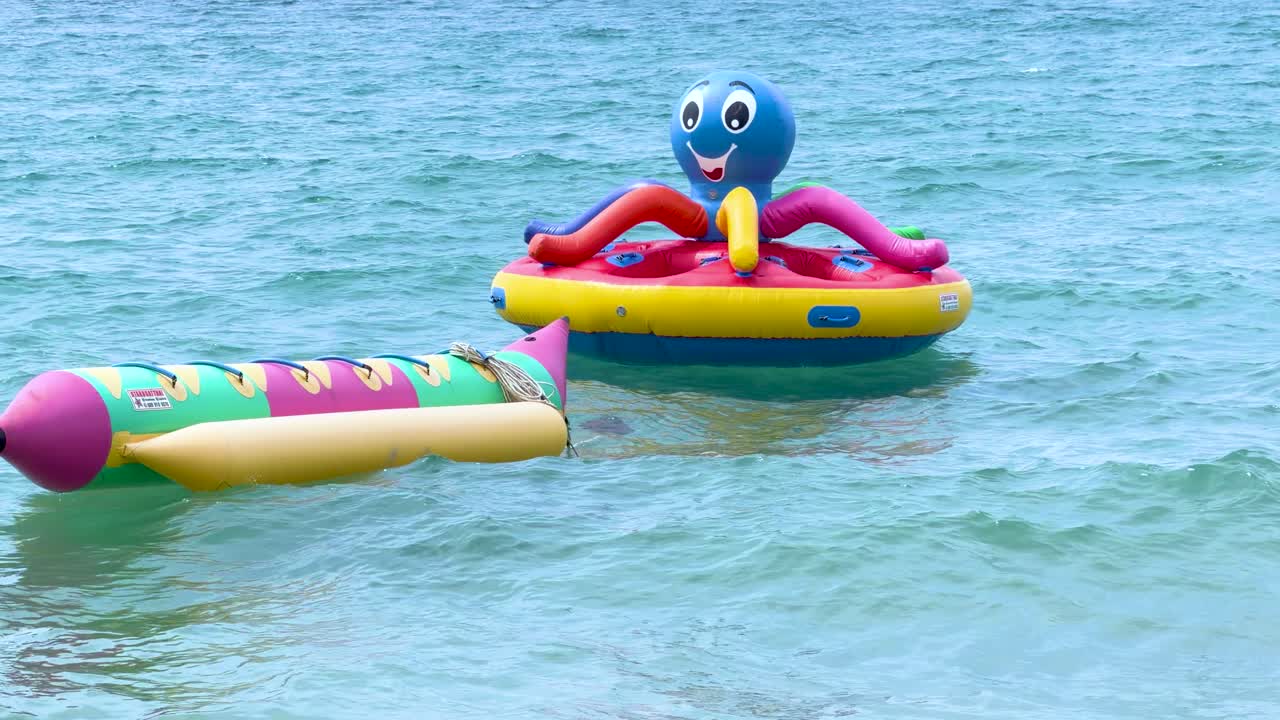Vibrant inflatable water toys float on calm turquoise ocean water under bright natural daylight