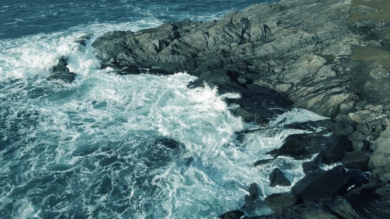 Stationary aerial shot of rocky irish shore line with waves pounding the rocks and coastline during cloudy day