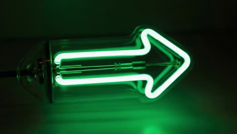 A striking green neon arrow illuminated in a dark environment, showcasing modern design and vibrant color that guides attention and signifies direction