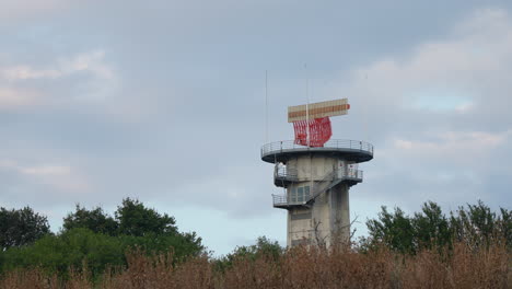 concrete radar tower with spinning antenna located near forested area under evening sky
