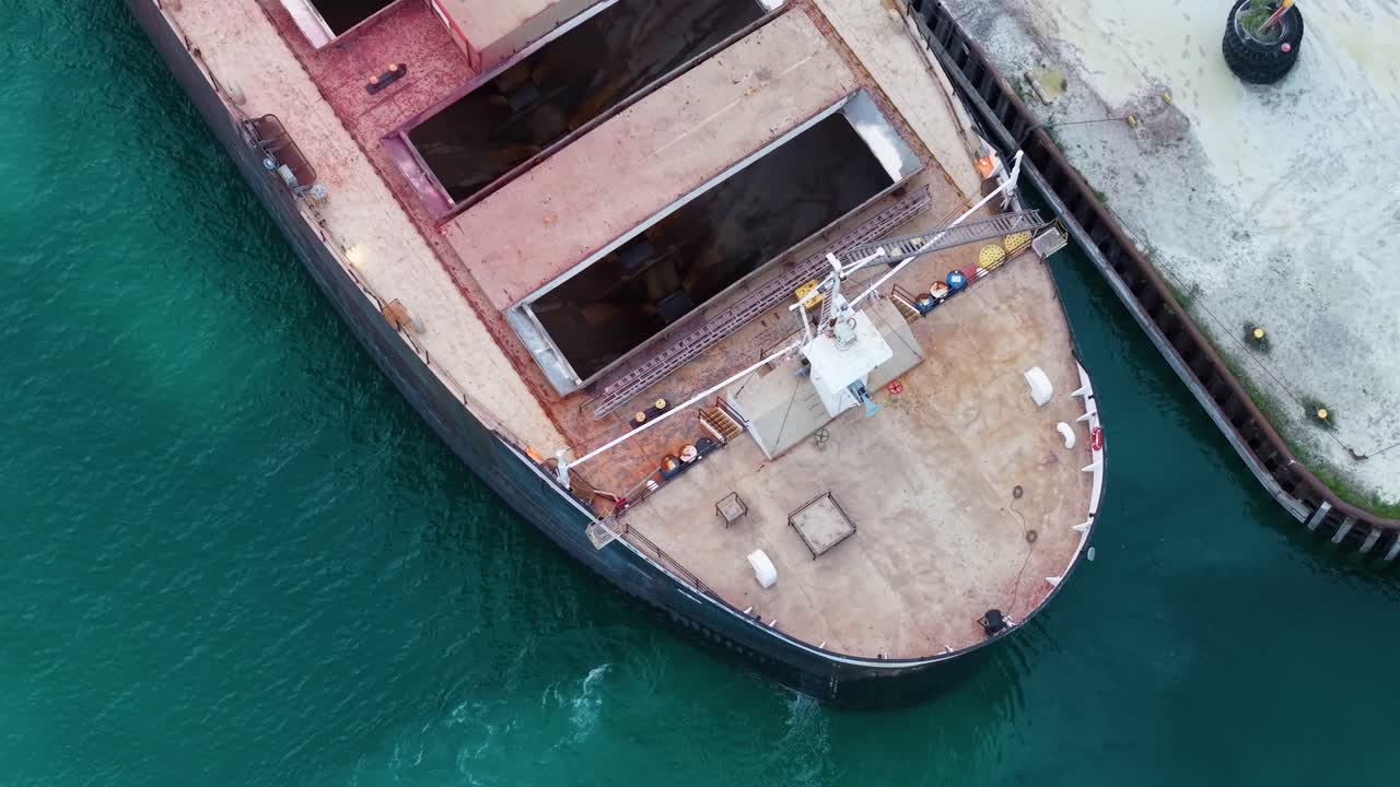 Aerial drone close-up view of a large cargo ship docked at an industrial pier over turquoise water