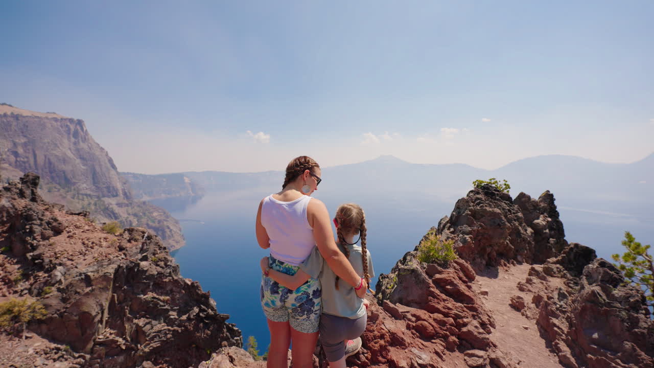 Mother and daughter admiring the scenic view of a vast lake and mountains
