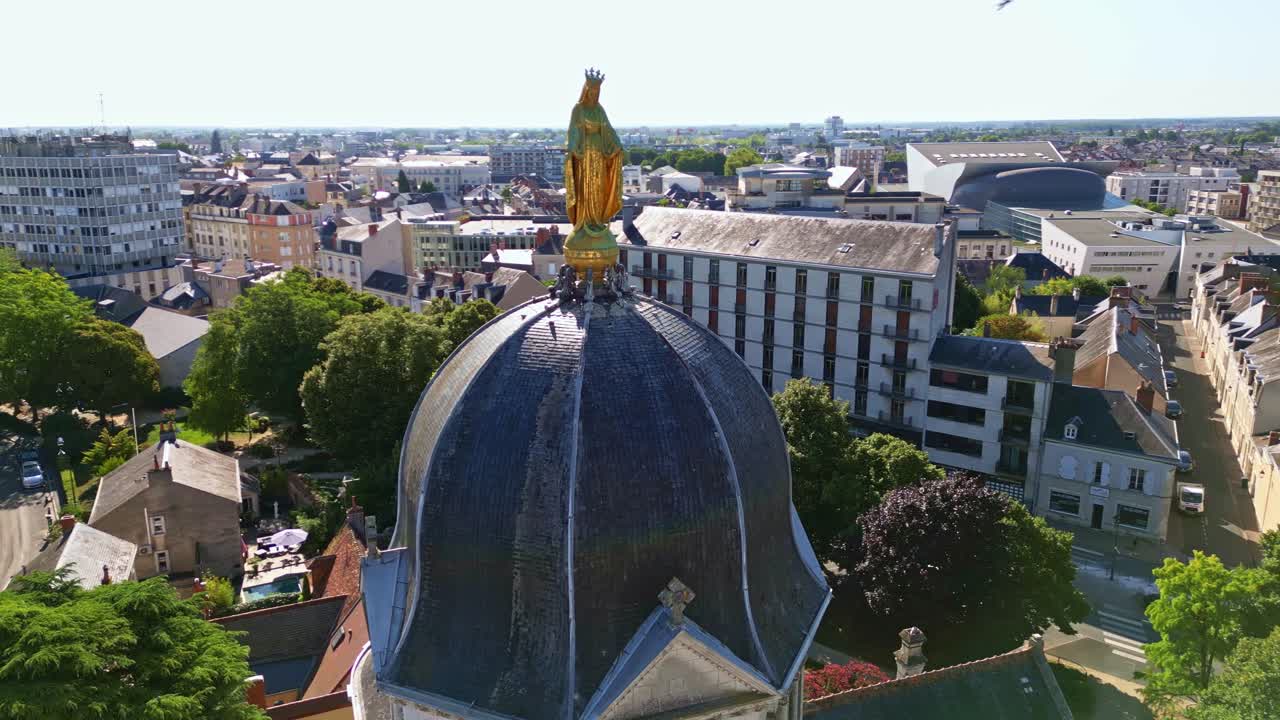 Golden Virgin Mary statue on dome of Église Notre-Dame de Châteauroux, cityscape in background, France. Aerial drone orbiting
