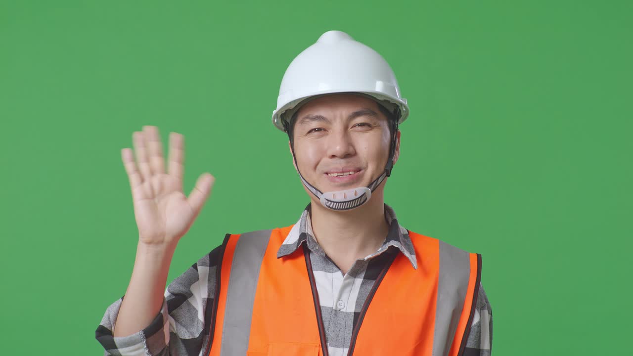 Close Up Of Asian Male Engineer With Safety Helmet Smiling To Camera And Waving Hand Saying Bye While Standing In The Green Screen Background Studio