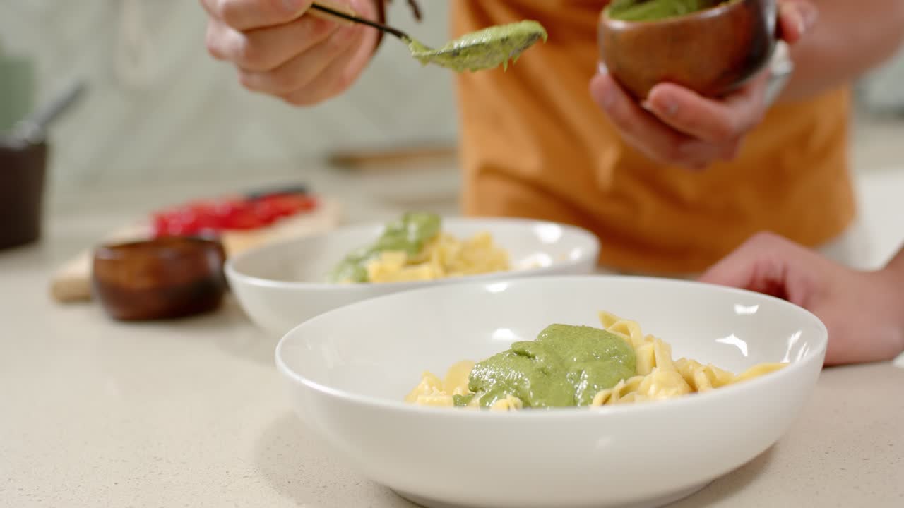 O cozinheiro está a mover e a servir molho verde na tigela da frente, na bancada, para finalizar o empratamento.