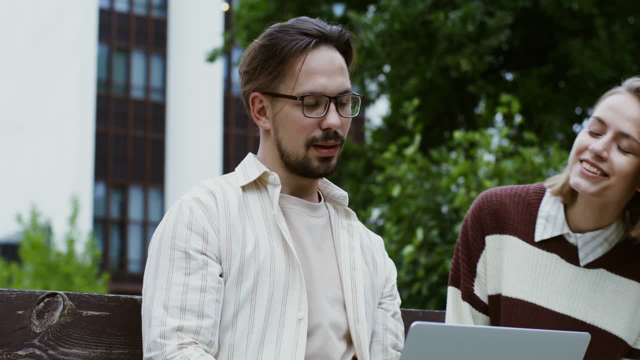 una pareja joven trabajando juntos en una computadora portátil afuera