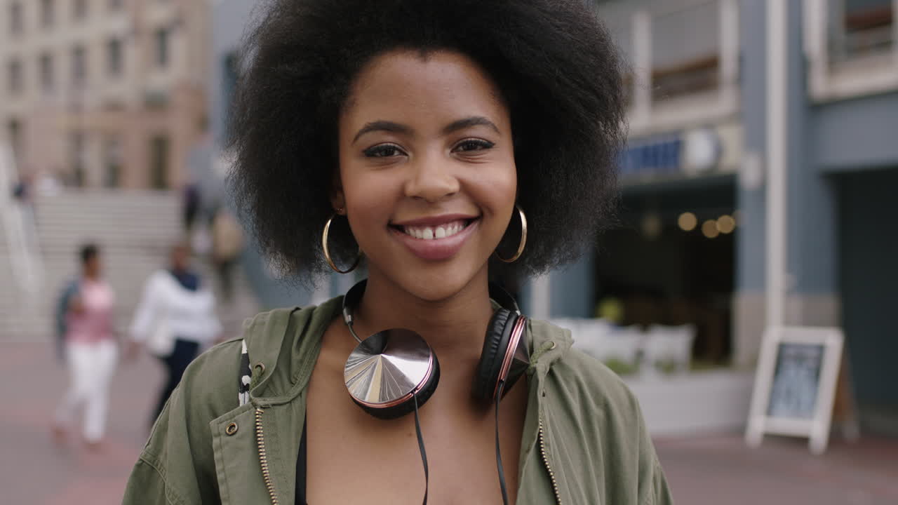 retrato en cámara lenta de una joven mujer afroamericana de moda con cabello afro rizado sonriendo feliz al aire libre urbano