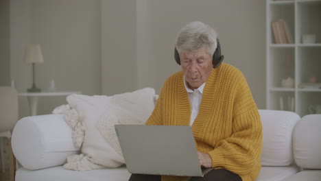 Eine-ältere-Frau-Mit-Grauen-Haaren-Führt-Zu-Hause-Einen-Videoanruf-Mit-Einem-Laptop-Durch.-Ältere-Frau-Führt-Einen-Videoanruf-Mit-Der-Familie,-Die-Lächelt-Und-Winkt.-Covid-19-Bleiben-Sie-In-Verbindung.-Online-Chat-Mit-Freunden