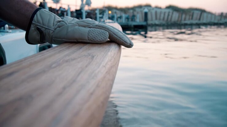 Un tramonto sereno riflesso sull'acqua calma con una mano guantata che riposa sulla ringhiera di legno della barca e conchiglie sulla riva sotto una marea calma.