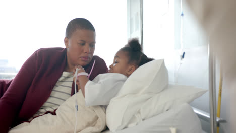 african american mother talking with daughter lying in hospital bed, slow motion