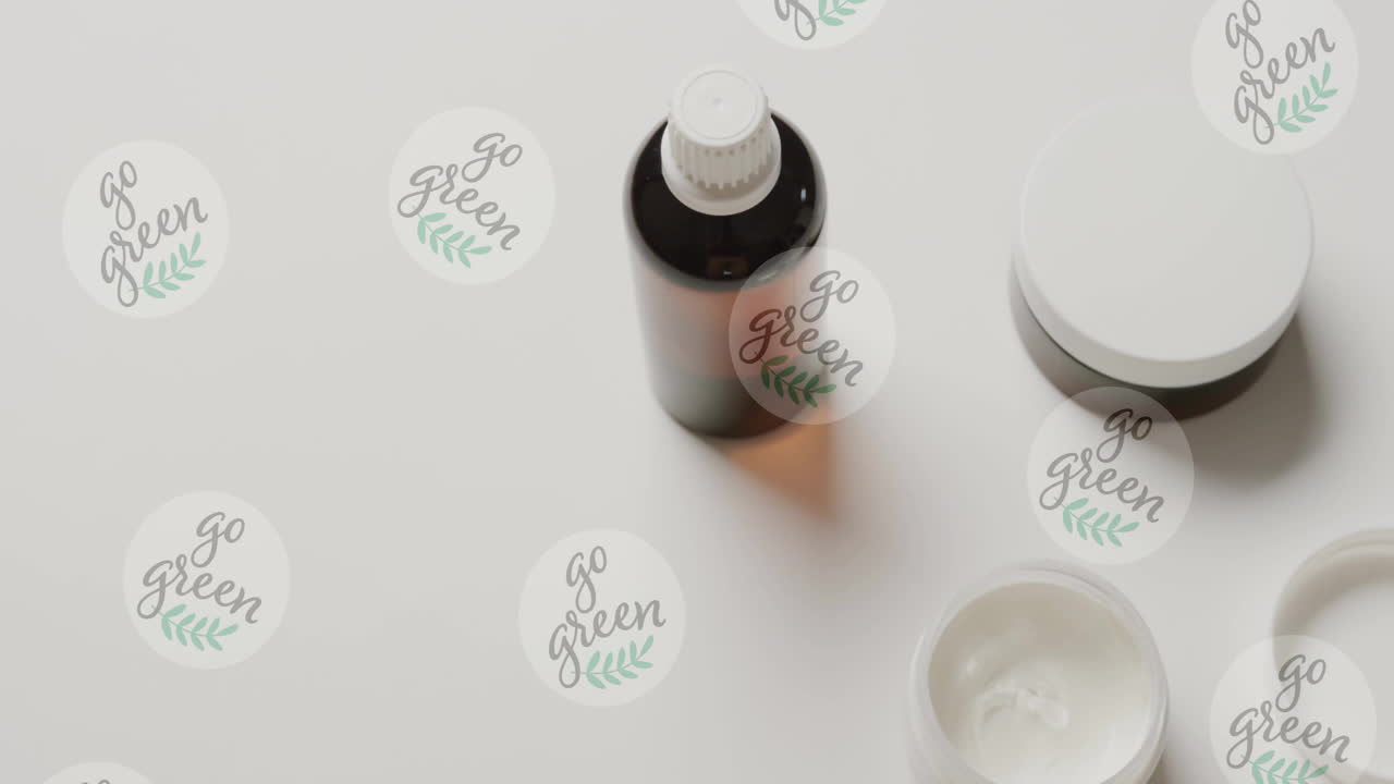 Animation of go green text and logos, over beauty cream jars and essential oil on white background