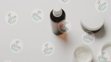 animation of go green text and logos, over beauty cream jars and essential oil on white background