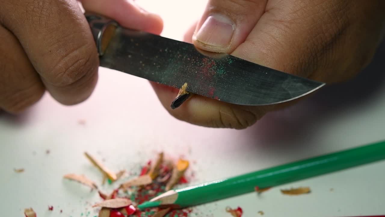 Opptak av hender som sakte spisser en blyant og noen fargeblyanter med en skarp kniv