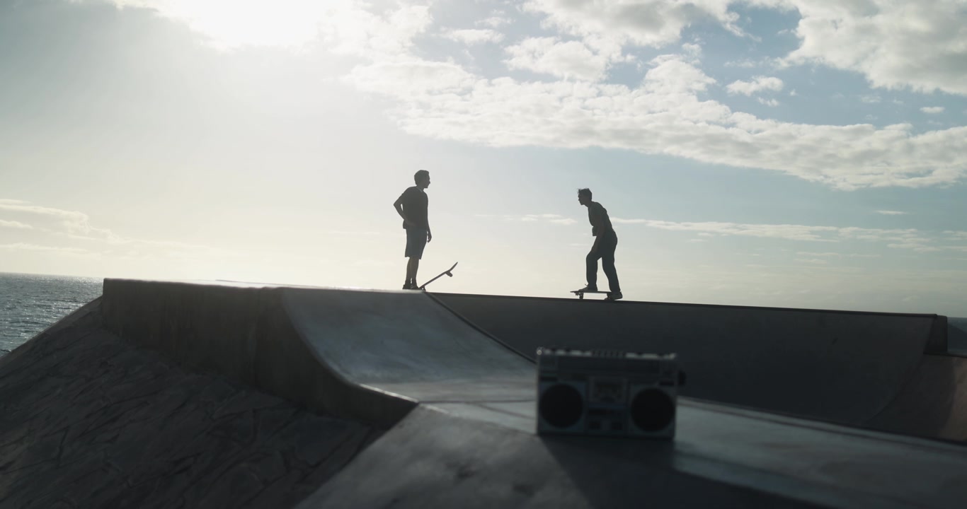 Sagome di giovani skater con boombox in uno skatepark costiero