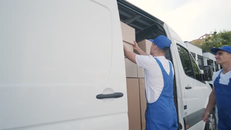 two young workers of removal company are loading boxes and furniture into a minibus